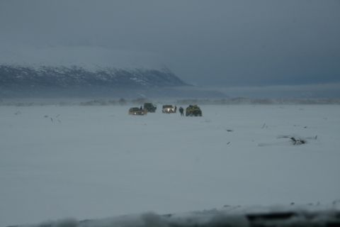1990 Chevrolet Suburban - Multiple SUVs traverse a snowy expanse with mountains in the distance under a gloomy sky.
