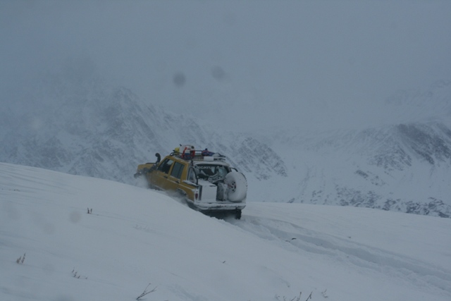 Yellow SUV with roof rack and spare tire on the back driving on a snowy mountain slope