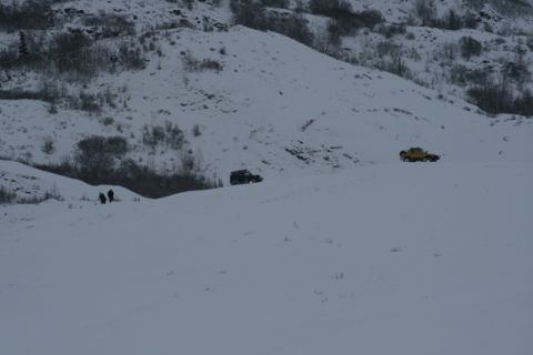 1990 Chevrolet Suburban - Two vehicles traverse a snowy terrain, with a group of people visible in the distance.