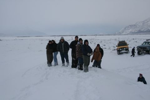 1990 Chevrolet Suburban - A group of people stand in a snowy field near two off-road vehicles under an overcast sky.