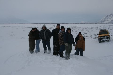 1990 Chevrolet Suburban - A group of people stand in a snowy landscape next to a yellow SUV that appears to be stuck in the snow.