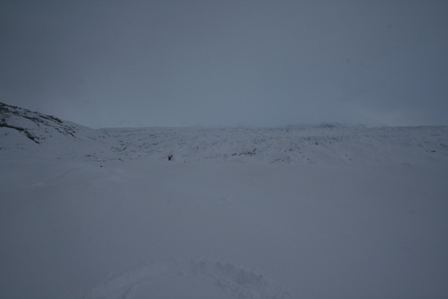 Snowy landscape with a person standing in the distance near a glacier