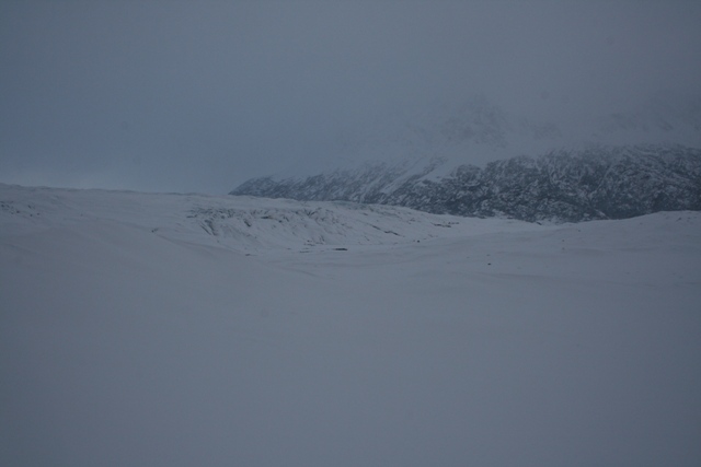 Snowy landscape with mountains in the background under a cloudy sky