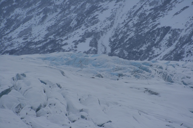 Snowy mountain slope above a textured glacier with blue ice visible in crevasses