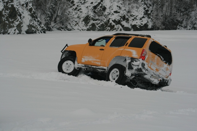 Orange SUV with roof rack stuck in deep snow, rear passenger side damaged