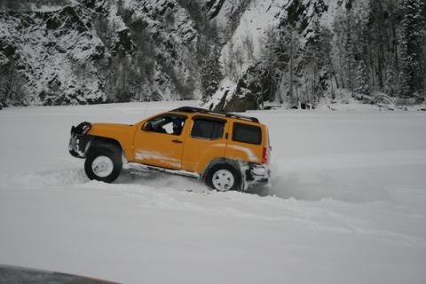 1990 Chevrolet Suburban - A yellow SUV navigates a snowy landscape with a mountainous, tree-lined backdrop.