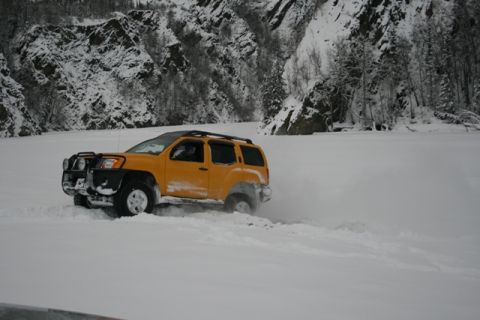 1990 Chevrolet Suburban - A yellow SUV navigates a snowy landscape with steep, tree-covered mountains in the background.