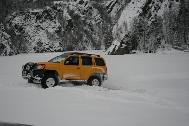 Yellow SUV driving through deep snow with a snowy mountain backdrop