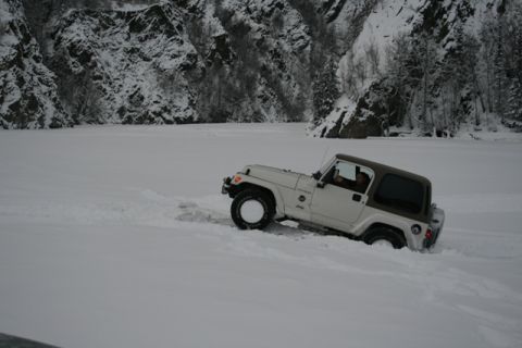 1990 Chevrolet Suburban - A Jeep navigates a snowy landscape with steep, tree-covered cliffs in the background.