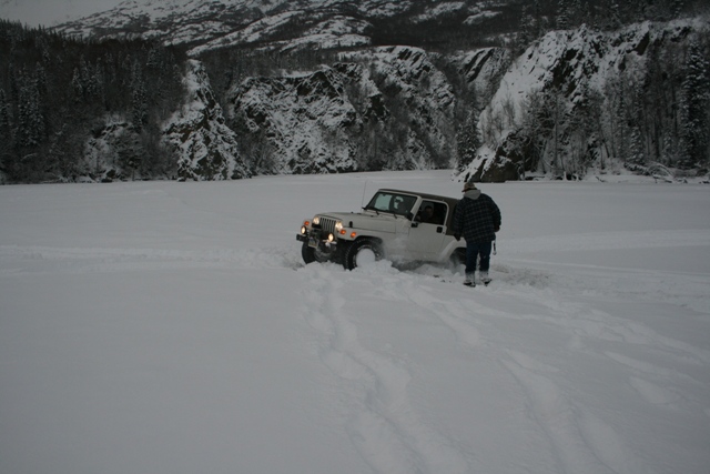 White Jeep Wrangler partially buried in snow, person in plaid jacket standing next to it