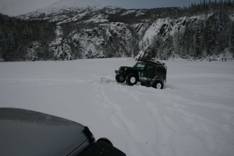 1990 Chevrolet Suburban - A dark green Jeep Wrangler navigates a snowy landscape, with another vehicle partially visible in the foreground.