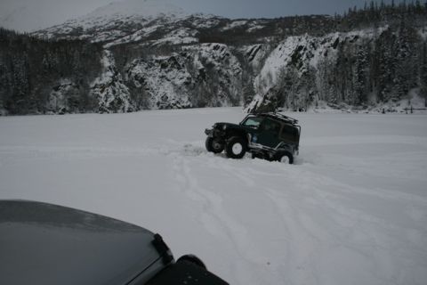 1990 Chevrolet Suburban - A dark green Jeep Wrangler navigates a snowy landscape, with a portion of another vehicle visible in the foreground.