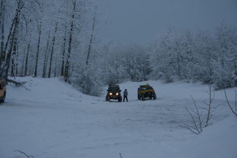 1990 Chevrolet Suburban - Two off-road vehicles are parked in a snow-covered forest clearing with a person standing between them.