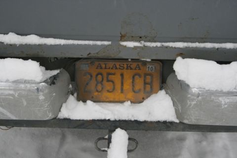 1990 Chevrolet Suburban - An Alaska license plate is partially obscured by snow, attached to a vehicle's rear.