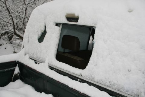 1990 Chevrolet Suburban - A snow-covered truck cab interior is visible through a window, with the dark green truck bed also covered in snow.