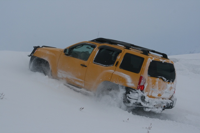 Yellow SUV kicking up snow while driving on a snowy slope