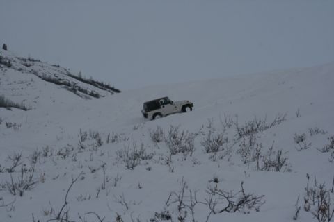 1990 Chevrolet Suburban - A white Jeep Wrangler navigates a snow-covered slope under a cloudy sky.