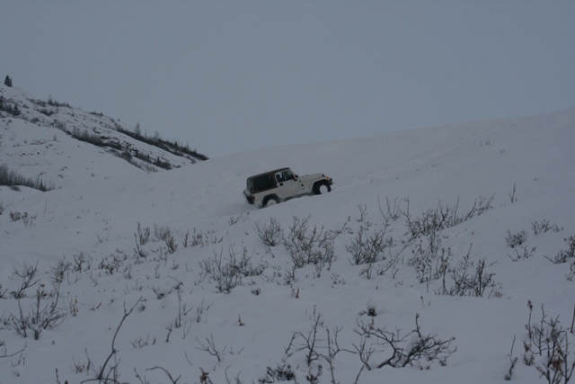 White Jeep Wrangler driving up a snowy hill on an overcast day