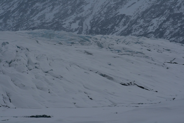 Snow-covered glacier with icy ridges and a mountain in the background