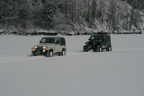 1990 Chevrolet Suburban - Two Jeep Wranglers navigate a snow-covered area, leaving tracks behind them.