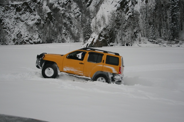 Yellow SUV driving through deep snow near a snowy mountain