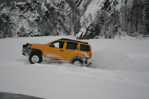 1990 Chevrolet Suburban - A yellow SUV navigates a snowy landscape, kicking up snow as it drives.