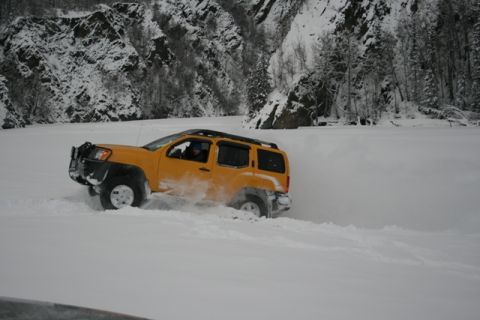 1990 Chevrolet Suburban - SUV navigating a snowy landscape with steep, tree-covered mountains.