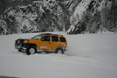 1990 Chevrolet Suburban - A yellow SUV navigates a snowy landscape near a rocky, tree-covered mountainside.