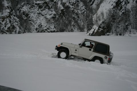 1990 Chevrolet Suburban - A white Jeep Wrangler navigates through a snowy landscape with rocky, snow-covered mountains in the background.