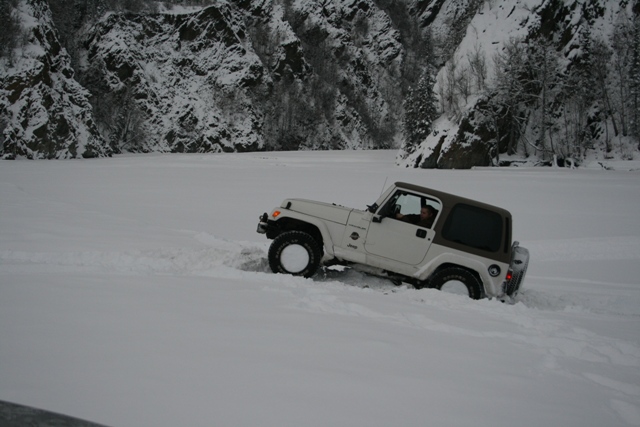White Jeep Wrangler driving through deep snow with a brown hardtop
