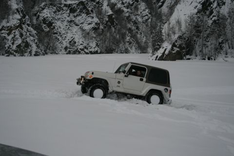 1990 Chevrolet Suburban - Jeep Wrangler navigating a snowy landscape with steep, wooded cliffs in the background.
