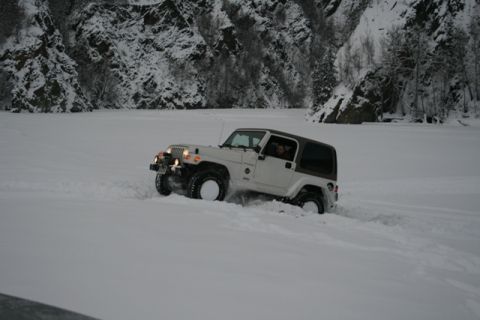 1990 Chevrolet Suburban - A Jeep navigates a snowy landscape, kicking up snow as it goes.