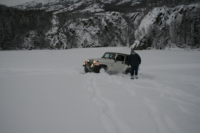 White Jeep Wrangler stuck in snow with person nearby