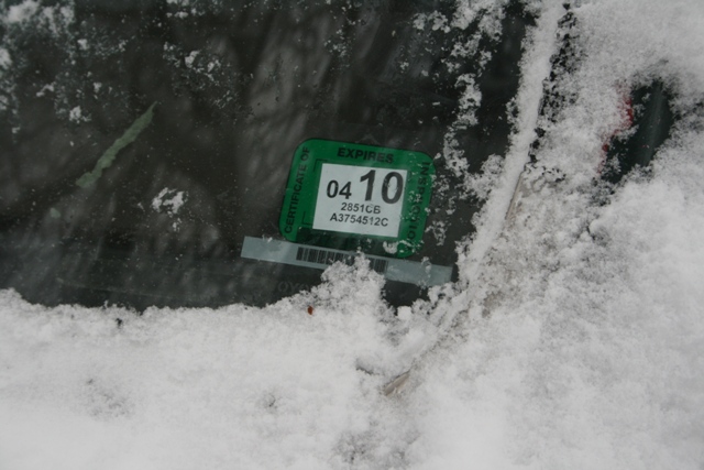 Green registration sticker with 'EXPIRES 04 10' on a snow-covered windshield