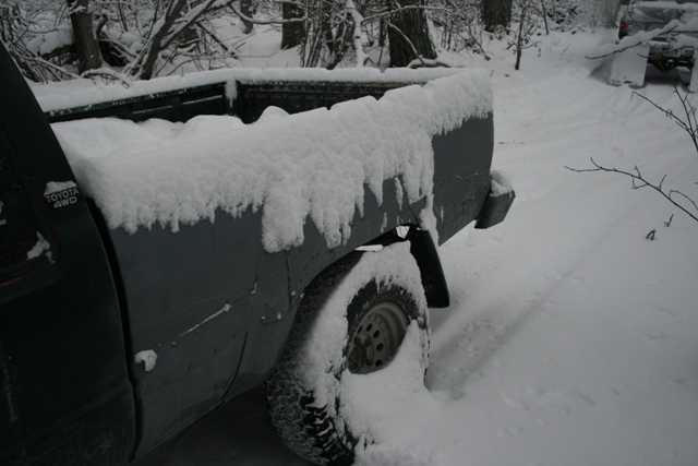 Toyota 4WD pickup truck bed and rear wheel covered in snow; another vehicle visible in background