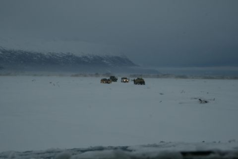 1990 Chevrolet Suburban - Several SUVs traverse a vast, snow-covered plain under a cloudy sky, with a mountain range visible in the distance.