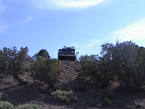 1991 Ford Bronco - A dark-colored off-road vehicle ascends a steep, rocky incline under a clear blue sky.