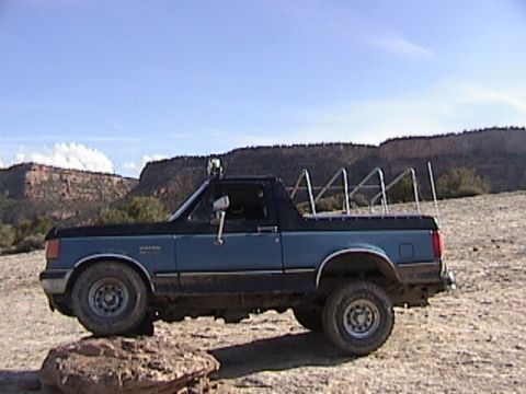 1991 Ford Bronco - This 1991 Ford Bronco is captured in a side profile, parked on terrain with a clear blue sky overhead.