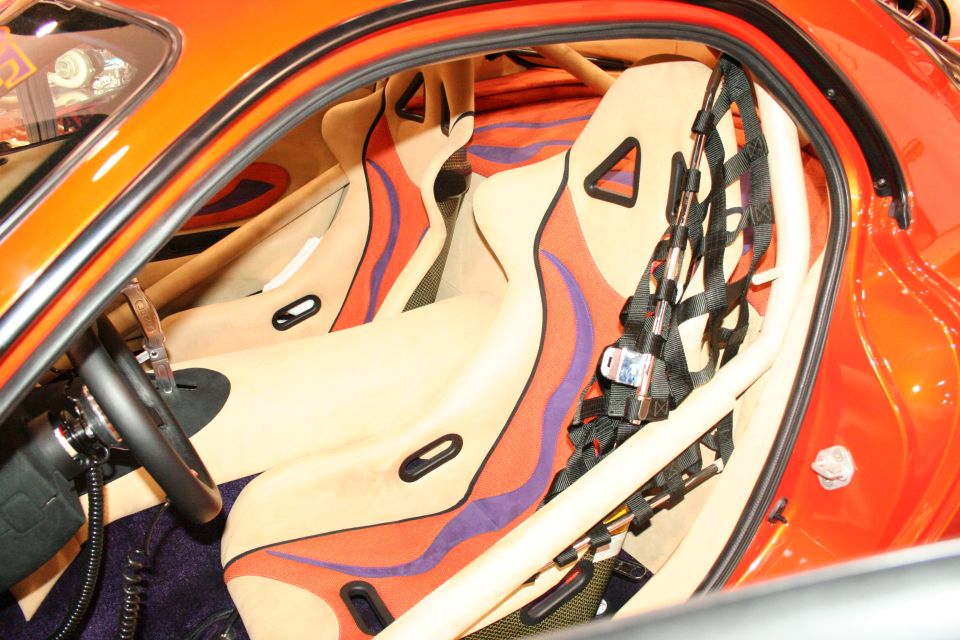 Interior view of racing seats with custom orange, purple, and red flame-like upholstery and a roll cage