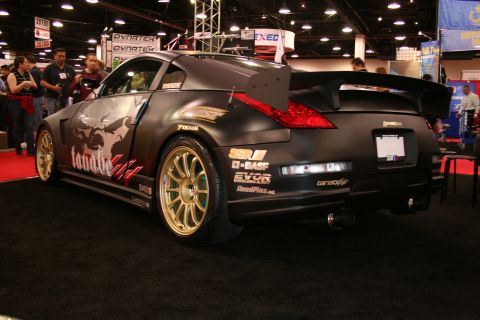 Modified black Nissan 350Z with gold rims and a large rear spoiler on display