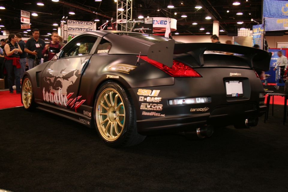 Modified black Nissan 350Z with gold rims and a large rear spoiler on display
