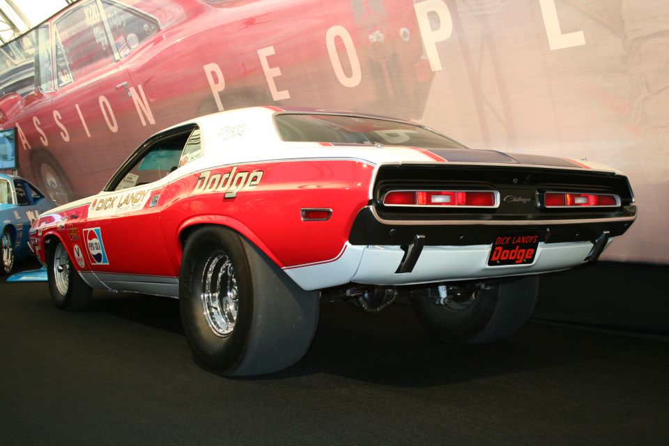 Rear view of a red and white Dodge Challenger drag car with wide rear tires. Dick Landy branding visible