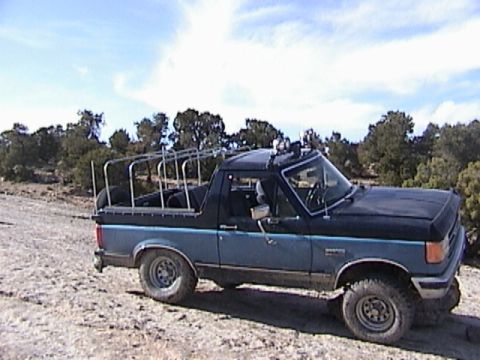 1991 Ford Bronco - 1991 Ford Bronco with custom roll cage and auxiliary lights parked off-road.