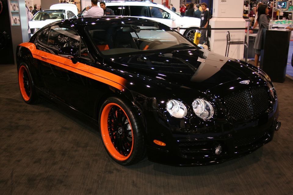 Black Bentley Continental GT with orange racing stripes and rims, seen at an indoor car show
