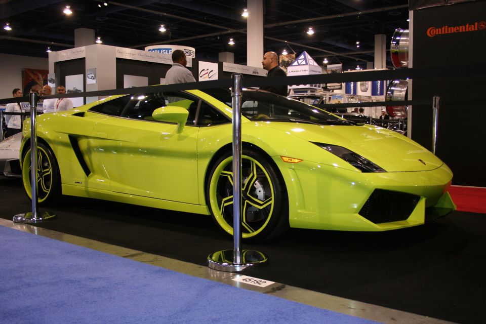 Lime green sports car with custom wheels and black accents, viewed from the front three-quarter angle at an indoor event