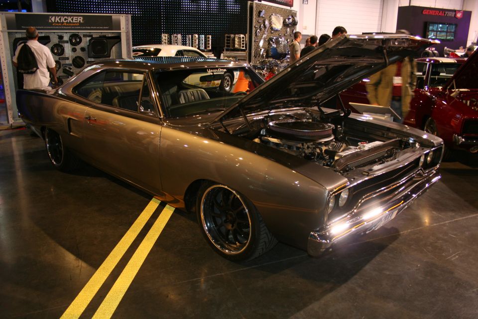 Brown muscle car with hood open, custom wheels, and yellow floor lines