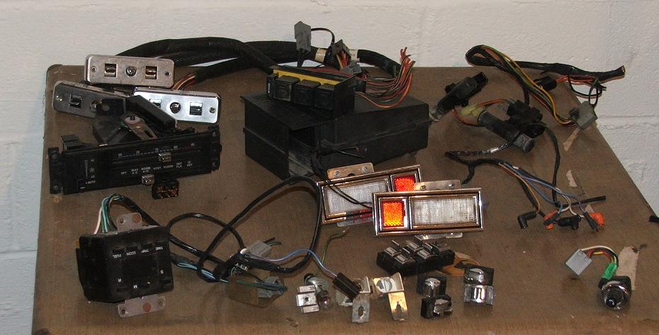 Various car parts including a fuse box, switches, and tail lights laid out on a table