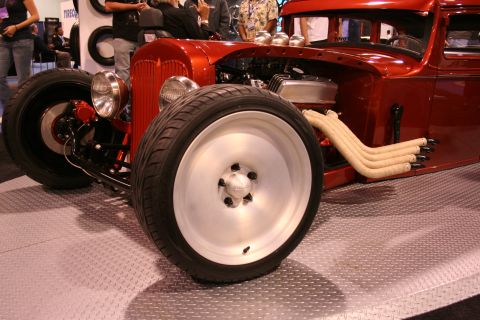 Front view of a red custom hot rod with a V8 engine, chrome exhaust headers, and large front wheels