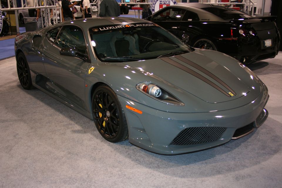 Gray Ferrari F430 with dark racing stripes and yellow brake calipers, front 3/4 view