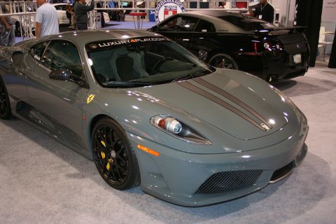 Gray Ferrari F430 with racing stripes on hood, black wheels, and yellow brake calipers. Black Nissan GT-R in b